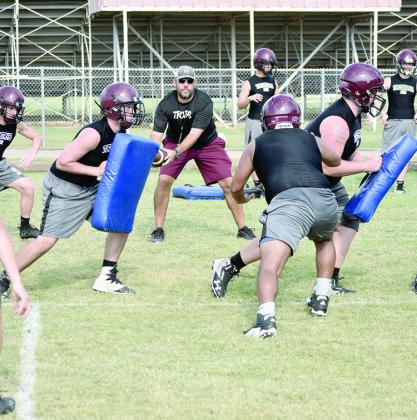 Cumby head coach Tom Dracos (center) plays the role of scout team quarterback during the first day of two-a-days Monday afternoon. The Trojans started practice with work on defensive alignments and offensive and defensive line schemes.