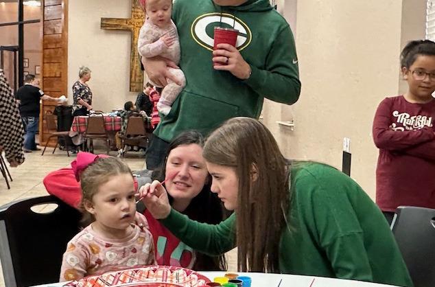Amerson Boles, a Sulphur Springs High School cheerleader, paints a candy cane face on Rebekah Newton, while parents Caroline and Matt Newton while baby sister, Marlee, watches.