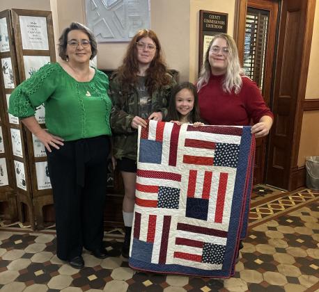Hopkins County Extension Agent Lisa Sprague along with Hopkins County 4-H members show off one of the qulits the youth have made for the Quilts of Valor project. Sprague updated Hopkins County Commissioners Court during a recent meeting about the club's taking on the project. Courtesy photos