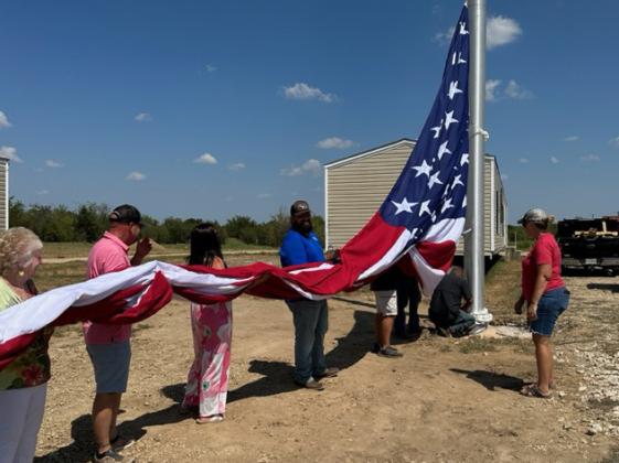 Roy Henly (second from left), family and employees keep the oversized USA flag from touching the ground as it is installed on the 100-foot flagpole at Henly Homes on Aug. 29. Staff photo by Enola Gay Mathews